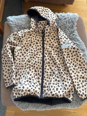 Leopardmönstrad beige vindjacka - Cool beige vindjacka med leopardmönster och huva. Jackan har hel dragkedja framtill och två snedställda fickor med dragkedja. Perfekt för dig som vill sticka ut och hålla dig varm under blåsiga dagar.