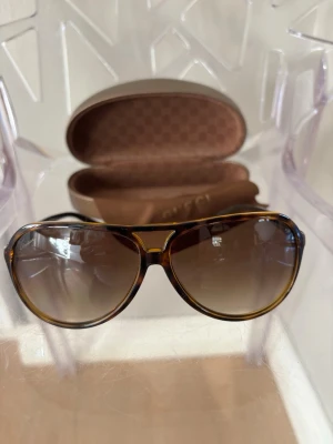 Bruna aviator-solglasögon från Gucci - Snygga aviator-solglasögon från Gucci med brun tonade glas och klassisk brunmelerad båge. Glasögonen har en elegant form och kommer med ett exklusivt fodral. Perfekt för dig som vill ha en cool och tidlös look. Kvitto, alla tags och originalaskar ingår
