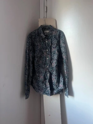 Morris skjorta - Snygg långärmad skjorta med blommigt mönster i mörkblå, gröna och vinröda toner. Skjortan har klassisk krage och knäppning framtill med vita knappar. Perfekt för dig som vill sticka ut lite extra med en färgglad och detaljerad look.