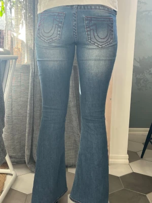 Blå bootcut jeans från True Religion - Säljer ett par blå bootcut jeans från True Religion broderade bakfickor. Jeansen har en lätt utsvängd passform och låg midja.💗💗