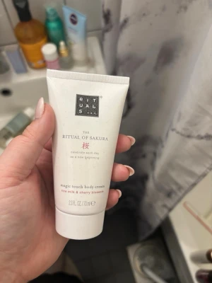 Rituals The Ritual of Sakura body cream - Lyxig body cream från Rituals i serien The Ritual of Sakura. Innehåller risextrakt och körsbärsblomma som ger en mjuk och återfuktande känsla. Vit tub med silverdetaljer och rosa text, 70 ml. Perfekt för dig som vill ha en fräsch och blommig doft.