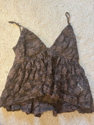 Brun topp  från Amisu - Säljer en brun topp från Amisu med justerbara axelband och v-ringad hals. Bodyn har ett blommigt spetsmönster. Har tagit bort lappen så det står ingen storlek men skulle gissa att den är i Xs