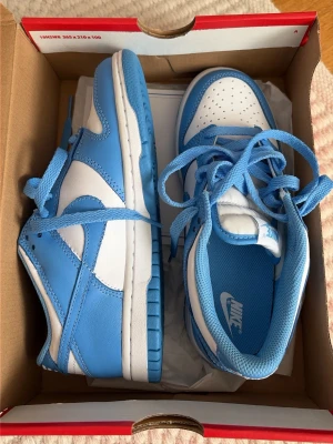 Nike Dunk Low blå/vit sneakers - storlek 35,5, aldrig använda förutom inomhus fram och tillbaks, säljer då de är för små för mig! går att diskutera ifall lådan ska följa med eller inte, för att underlätta skornas resa