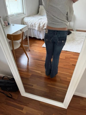 Blå bootcut jeans från True Religion - Säljer ett par blå bootcut jeans från True Religion i storlek 28. Jeansen har låg midja och detaljerade bakfickor med knappar. 