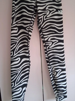 Zebramönstrade leggings från 157 - Snygga zebramönstrade leggings från 157 i svart och vitt. De är tighta och har ett coolt djurmönster som verkligen sticker ut. Perfekta för dig som vill ha något unikt och trendigt. Materialet är stretchigt och bekvämt, passar bra till både träning och chill.