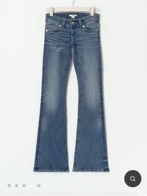 Blå low rise jeans från Gina 14+ - Säljer ett par blå bootcut jeans med lätt slitning och en liten ripped-detalj på låret. Jeansen har klassisk femficksmodell, låg midja och är tillverkade i denim med stretch. Perfekta för dig som gillar en retro vibe och vill ha ett par jeans som sticker ut.