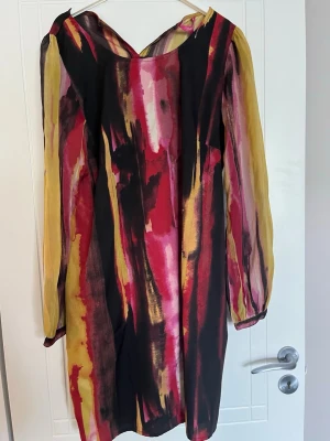 Färgstark långärmad klänning/tunika Indiska - Unik klänning/tunika från Indiska i storlek L med långärmad design och färgstarkt abstrakt mönster i svart, rött, gult och rosa. Luftigt material och lös passform, perfekt för dig som gillar att sticka ut med din stil. Knapp saknas i nackknäppningen. 