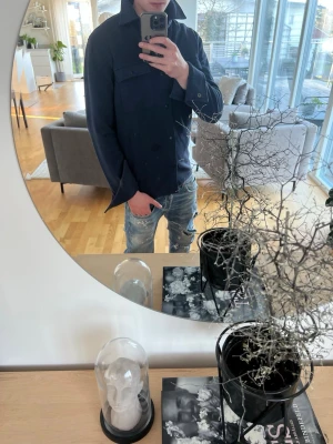 Mörkblå overshirt från select home  - Stilren mörkblå overshirt från select home  med klassisk krage, två bröstfickor med lock och knappar samt knappstängning framtill. Tillverkad i ett mjukt, tjockare tyg som ger en avslappnad men ändå snygg look. Perfekt att bära över en t-shirt eller hoodie.