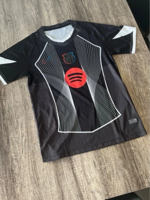 FC Barcelona Nike matchtröja - Snygg svart FC Barcelona matchtröja från Nike med vita och röda detaljer samt Spotify-logga på bröstet. Tröjan har korta ärmar, grafiskt mönster framtill och klubbmärke i svart, rött och blått. Perfekt för fotbollsträning eller att bära till vardags. Finns hemma fraktar inom en dag!!!