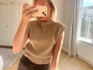 Beige ribbad ärmlös topp💖💖 - Säljer en beige ribbad topp med hög hals och ärmlös design. Perfekt för att skapa en clean och stilren look. Materialet är mjukt och stretchigt, vilket gör den bekväm att bära. Passformen är normal och toppen är något croppad. ( lite dåligt skick - sista bilderna)