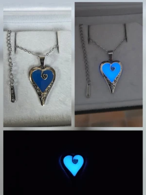 Glow in the dark hjärthalsband blå - Unikt handgjort halsband med hjärtformat hänge i blått som lyser i mörkret. Hänget är ca 2,5 cm och har silverfärgad metall med dekorativa snirkliga detaljer. Kedjan är tunn och silverfärgad i rostfritt stål med justerbar längd. Perfekt för dig som gillar coola accessoarer med lite magisk känsla. Effekten aktiveras av vanligt dagsljus och solljus, lyser i flera timmar vid normal användning. Lång livslängd, både kedjan & hänget tål vatten o missfärgas ej. 