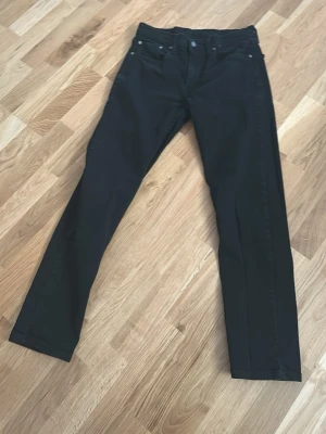 Svarta raka jeans - Säljer ett par svarta jeans med rak passform och klassisk femficksdesign. Jeansen har knapp- och dragkedjegylf samt bälteshällor. Materialet är denim och färgen är djup svart, perfekt för en stilren look. Levis 502. Är små för storleken 