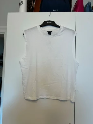 Vit ärmlös topp från Lindex - Säljer en enkel och stilren vit ärmlös topp från Lindex. Toppen har rund halsringning och är gjord i mjuk bomull, perfekt för att matcha med jeans eller shorts. Passformen är normal och den är riktigt bekväm att bära.