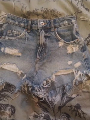 Jeansshorts med hög midja och slitna detaljer Bershka - Ett par ljusa jeansshorts med hög midja i storlek 34. Väldigt fina, knappt använda. Fem ficksmodell.
