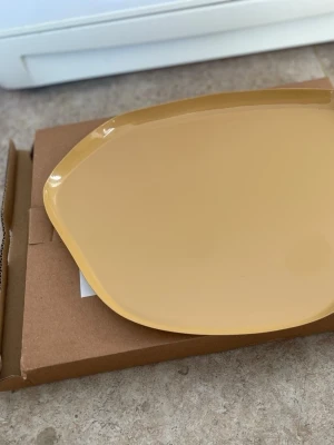 Gul oregelbunden tallrik - En snygg gul tallrik med oregelbunden form och blank yta. Perfekt för att servera mat eller snacks på ett unikt sätt. Tallriken är tillverkad i keramik och har en modern design som sticker ut på bordet.