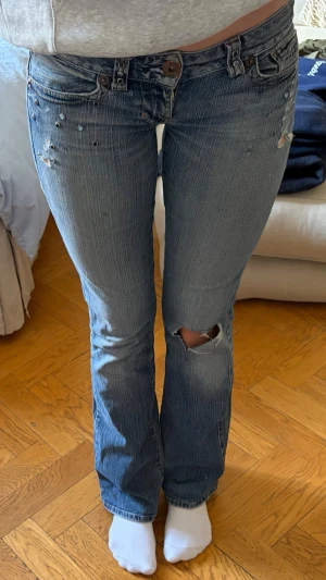 Low waist Guess jeans  - Säljer ett par blå bootcut jeans köpta på secondhand i New York! Jeansen har ett hål på höger knä och ”nitar” eller strass vid framfickorna (se bild 3). Midjemått syns på bild 4 och innerbenslängd på bild 5! Bakfickorna har slitningar. Hör av dig vid frågor! 