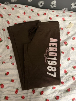 Bruna mjukisbyxor Aeropostale M - Bruna mjukisbyxor från Aeropostale med tryck 'AERO1987 New York' i rosa och vitt på benet. Byxorna har fit & flare-modell och dragsnöre i midjan. Kan tänka sälja den matchande tröjan för 250 kr till