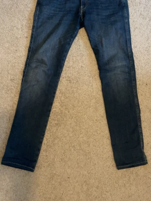 Blå jeans från Replay - Snygga blå jeans från Replay i slim fit-modell. Klassisk femficksdesign med dragkedja och knapp framtill. Jeansen har en mörk tvätt och är tillverkade i bomull med en skön stretch. Perfekta för en avslappnad och trendig look. Storlek 32W 34L