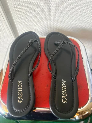 Svarta flätade sandaler från Fashion - Stilrena svarta sandaler från Fashion med tunna, flätade remmar och klassisk flip-flop design. Tillverkade i syntetmaterial med mjuk sula för extra komfort. Perfekta för varma dagar och enkel att matcha med olika outfits.