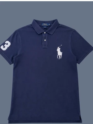 Marinblå pikétröja från Polo Ralph Lauren - Klassisk marinblå pikétröja från Polo Ralph Lauren med vit broderad logga på bröstet och siffran 3 på ärmen. Tröjan har krage, korta ärmar och knäppning framtill. Perfekt för en stilren och sportig look.