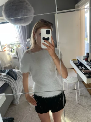 Vit fluffig topp med kort ärm - Supermjuk och fluffig vit topp med korta ärmar och rund hals. Toppen har en figurnära passform och är perfekt för dig som gillar en mysig och trendig look. Materialet är syntetiskt och ger en cool, lite lurvig känsla.