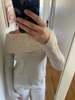 Beige off shoulder stickad tröja - Säljer en beige stickad tröja med bred off shoulder-krage och långa ärmar. Tröjan har ribbstickade muddar vid ärmslut och nederkant. Perfekt för dig som gillar en avslappnad men ändå trendig stil.