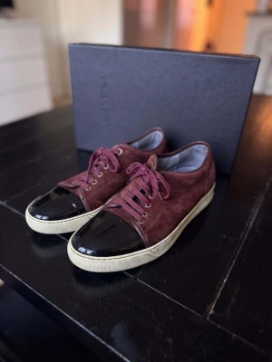 Lanvin DBB1 Cap Toe Sneaker – Svart | Strl 44 | Mycket Gott Skick - Lanvin DBB1 Cap Toe i klassisk svart — ikonisk fransk lyx med patent läder finish och signatur cap toe design. ⚠️ Storleksguide: Denna modell är stor i storleken. Strl 44 passar som 45. Mycket gott skick med minimalt slitage. ✅ Skriv i DM för kvitto — vi håller det privat för att skydda köparens personliga information Storlek 44. Vi tar även emot byten och uppgraderingar. Kan även köpas via www.nordens.store med Klarna & Paypal. Vi reparerar, renoverar & rengör även skor,  skriv i DM! 👟 📦 Spårad 