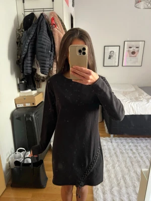 Svart långärmad klänning med snörning - Svart enkel och stilren klänning med lång ärm och rund halsringning. Klänningen har en snygg snörningsdetalj nertill på ena sidan som ger en cool touch. 