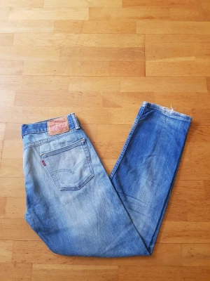 Levi's 513  - Säljer ett par klassiska Levi's 513 jeans i ljusblå denim med raka ben och femficksmodell. Jeansen har en snygg vintage tvätt och ikonisk läderpatch bak i midjan. Materialet är 100% bomull och de har den typiska röda Levi's-taggen på bakfickan.