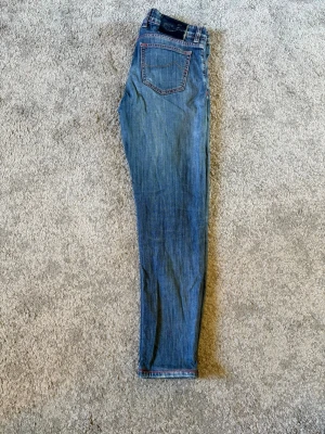 Blåa jeans från Jacob Cohën  - Snygga blå jeans från Jacob Cohën med klassisk femficksdesign och röda sömmar. Jeansen har en smal passform och normal midja. Perfekta för dig som gillar en tidlös och trendig look. Är även hål på båda knäna från början när dessa köptes