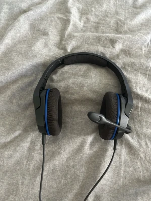HyperX gamingheadset med mikrofon - Säljer ett svart HyperX gamingheadset med blå detaljer och inbyggd mikrofon. Over-ear-modell med mjuka öronkuddar och justerbart huvudband. Perfekt för gaming och voicechat. Ansluts med kabel.