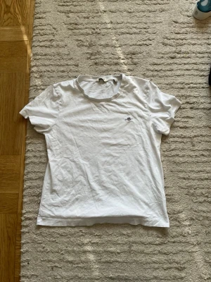 Vit t-shirt från GANT med broderad logga - Klassisk vit t-shirt från GANT med rund halsringning och liten broderad logga på bröstet. T-shirten är enkel och stilren, perfekt till jeans eller shorts. Tillverkad i mjuk bomull för en skön känsla. Storlek M i barn 
