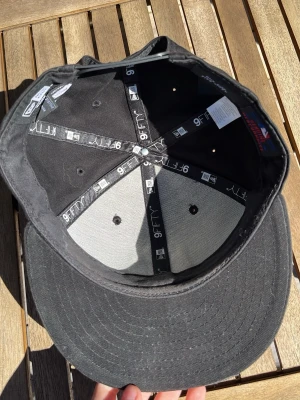 Svart keps New Era 9FIFTY snapback - Svart keps från New Era, modell 9FIFTY snapback. Klassisk form med platt skärm och justerbar plastrem bak. Tillverkad i bomullstyg med broderade ventilationshål och märkning på insidan.