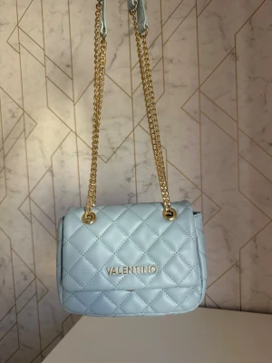 Ljusblå Valentino väska  - Snygg ljusblå axelväska från Valentino med quiltat mönster och guldfärgad kedjerem. Köpt i Italien och inte använd alls, helt ny! 🩵🩵🩵pris går att diskutera