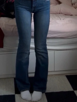 Blå bootcut jeans med hög midja - Säljer ett par klassiska blå bootcut jeans med hög midja och lätt slitna detaljer framtill. Jeansen har en tidlös tvätt och är tillverkade i ett mjukt denimtyg som sitter snyggt över höfterna och låren innan de blir vidare nedtill. Strl 40 men skulle säga att de passar M