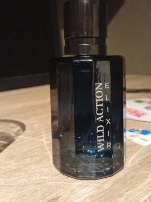 Wild Action Elixir parfym - Wild Action Elixir parfym i en mörkblå, åttakantig glasflaska med svart lock. Flaskan har en stilren design med texten tryckt i vitt längs sidan. Perfekt för dig som gillar en modern och cool look på parfymhyllan parfymen är typ inte använd. Skriv om ni har frågor Mvh Freke