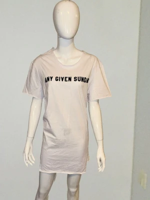 Oversized Eksi T-shirt ”Any Given Sunday” – XL - Cool oversized t-shirt i 100% mjuk bomull! ☁️ Vit med snyggt svart tryck och råa kanter vid ärmslut och nederkant för en avslappnad look. Den generösa längden gör den perfekt till leggings eller jeans! ​Märke: Eksi ​Storlek: XL ​Mått: Bröst 52 cm, Längd 78 cm ​Material: 100% Bomull 