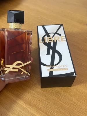 Yves Saint Laurent Libre Intense parfym - Säljer en lyxig Yves Saint Laurent Libre Eau de Parfum Intense. Flaskan är rektangulär med guldiga detaljer och svart lock, och doften kommer i en elegant svart och vit kartong med guldtext. Perfekt för dig som gillar exklusiva parfymer.