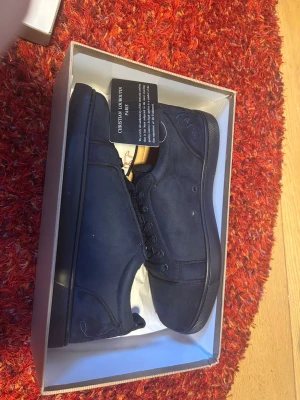 Mörkblå sneakers från Christian Louboutin - Snygga mörkblå sneakers från Christian Louboutin med klassisk röd sula och diskret logga på sidan. Skorna är i textil och har matchande mörkblå snörning. Perfekta för dig som vill ha en stilren och exklusiv look.