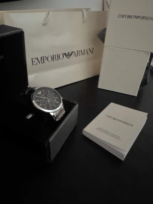 Emporio Armani silverfärgad klocka svart  - Stilren klocka från Emporio Armani med silverfärgat armband och svart urtavla. Klockan har flera små urtavlor och klassisk rund form. Perfekt accessoar för dig som gillar en elegant och modern look.