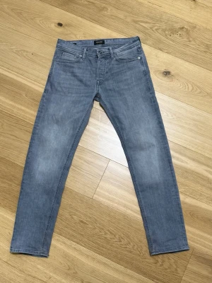 Grå jeans J&J - Snygga grå slim fit jeans från J&J med klassisk femficksdesign och diskreta slitningar. Jeansen är slim fit. Storlek 30 midja/32 längd