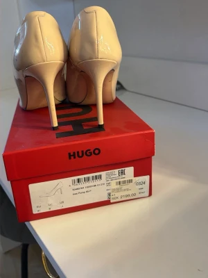 Beige pumps med spetsig tå från Hugo - Stilrena pumps i beige lack från Hugo med spetsig tå och hög smal klack. Skorna har en glansig finish och klassisk siluett som ger en elegant vibe. Perfekta för dig som gillar en clean och trendig look.