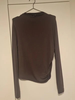 Brun långärmad topp med rynk - Mörkbrun långärmad topp med rund hals och snygg rynkdetalj på sidan. Tunn och mjuk i materialet, perfekt för lager-på-lager eller som den är. Enkel och stilren design som passar till många olika outfits.