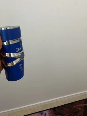 Blå parfymflaska Asad Lattafa - Snygg parfymflaska från Lattafa i en cool blå färg med silvriga detaljer och arabiska bokstäver. Flaskan har en modern, rundad form och känns lyxig med sin metallfinish. Perfekt för dig som gillar unika och stilrena dofter.