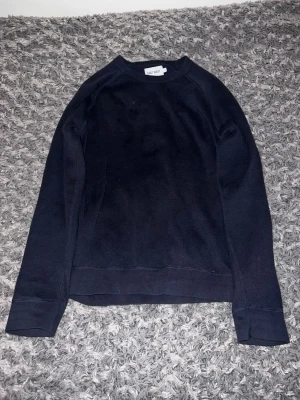Svart sweatshirt från East West - En stilren svart sweatshirt från East West med rund halsringning och långa ärmar. Tröjan har en klassisk passform och ribbade muddar vid ärmslut och nederkant. Perfekt för en avslappnad och enkel look.