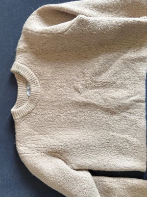 Beige stickad tröja från American Vintage - Mysig beige stickad tröja från and other stories med rund halsringning och ribbade muddar. Tröjan har en avslappnad passform och är tillverkad i en mjuk ullblandning som känns skön mot huden.