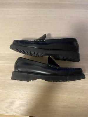 G.H. Bass Weejun  - Klassiska svarta loafers från G.H. Bass i blankt läder med grov sula och penny-detalj framtill. Snyggt sydda kanter och tidlös design som passar till många olika stilar.