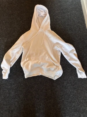 H&M Hoodie relaxed fit vit  - En klassisk vit hoodie med stor känguruficka framtill och justerbar huva med dragsko. Hoodien har ribbade muddar vid ärmslut och midja. Perfekt för en avslappnad och enkel stil. Hoodien har tyvärr mindre synliga fläckar på både fickan och på den vänstra armen ( Se bild 2 och 3). Tröjan är fortfarande väldigt bra för hemma bruk🤩 Tveka inte på att höra av dig för fler bilder eller frågor!