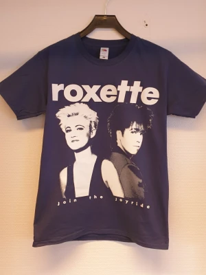 Roxette t-shirt mörkblå storlek Smal  - mörkblå t-shirt med Roxette-tryck och texten 'Join the Joyride' framtill. Klassisk passform med rund hals och korta ärmar. Perfekt för dig som gillar bandmerch och vill sticka ut med en ikonisk look.