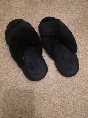 Mörkblå fluffiga tofflor med korsband - Mysiga mörkblå tofflor med korslagda band över foten och mjuk, fluffig yta. Från Nelly tror jag. Storlek 38. Inte mycket använda 